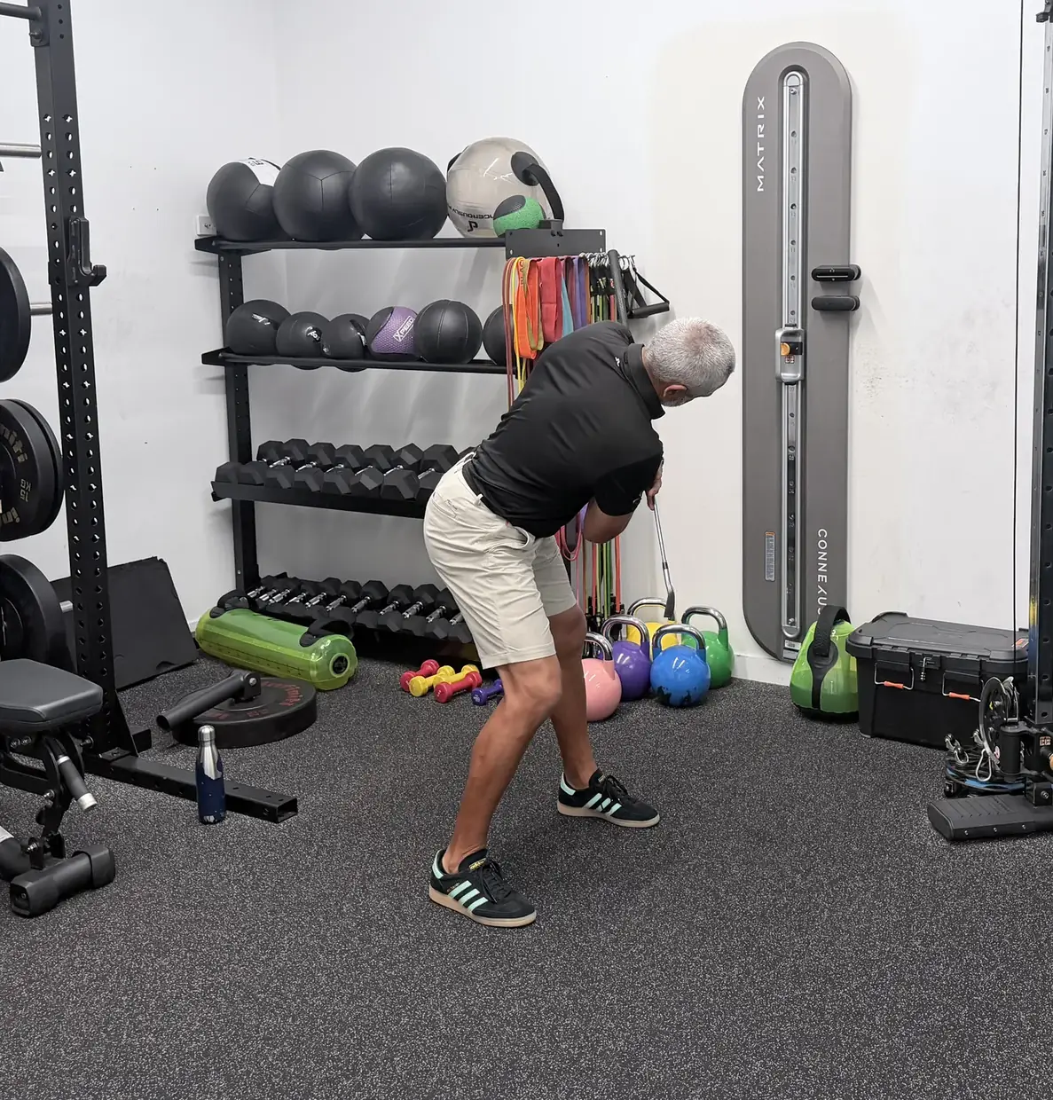 A golf physiotherapist set up in golf posture with a club at address, ready to make a practice swing